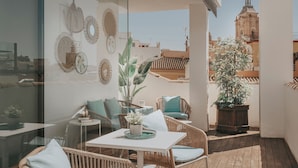 Un balcón con mobiliario de mimbre, una mesa y una planta en maceta.