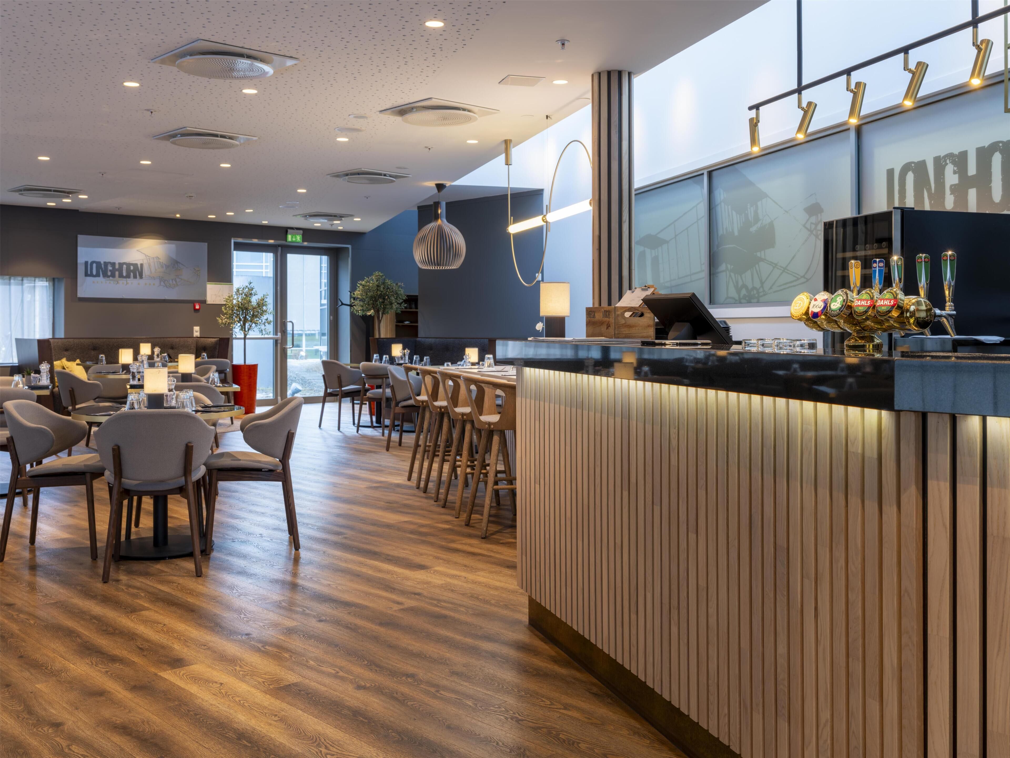 A modern hotel lobby with a bar area, seating arrangements, and a large window.