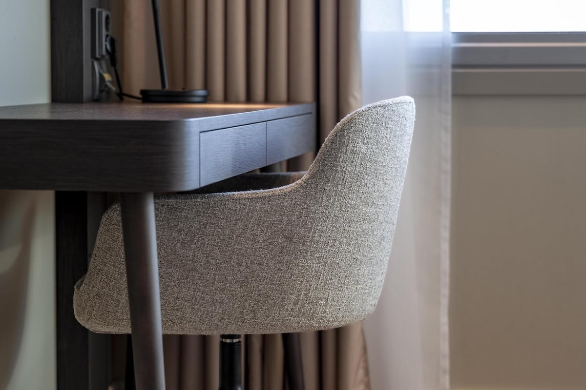 A modern office chair with a high backrest and metal legs, positioned next to a desk with a computer and a lamp.