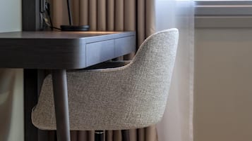 A modern office chair with a high backrest and metal legs, positioned next to a desk with a computer and a lamp.
