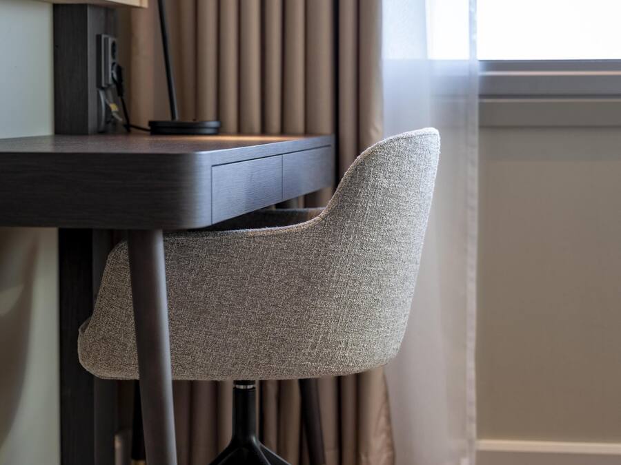 A modern office chair with a high backrest and metal legs, positioned next to a desk with a computer and a lamp.