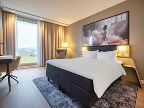 A hotel room with a large bed, a desk, a chair, and a view of the outdoors.
