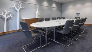 Ein Konferenzraum mit einem weißen Tisch, grauen Stühlen, einer Holzkabine und dekorativen Baumformen an der Wand.