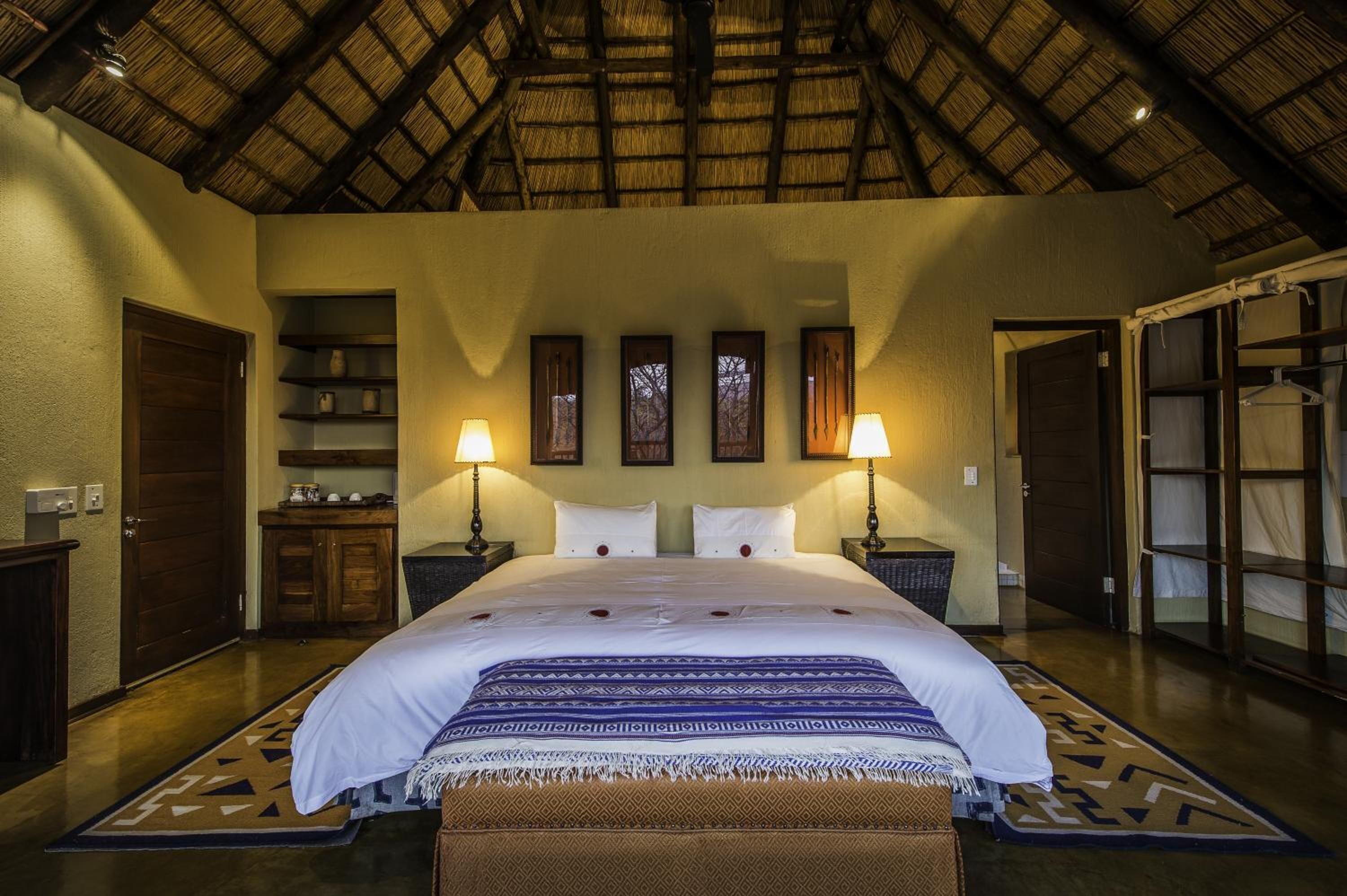 A spacious bedroom with a large bed, two bedside lamps, a wooden wardrobe, and a shelf with decorative items.