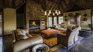 A cozy living room with a stone fireplace, leather sofas, and wicker chairs. - Tshwene Lodge (Vaalwater)