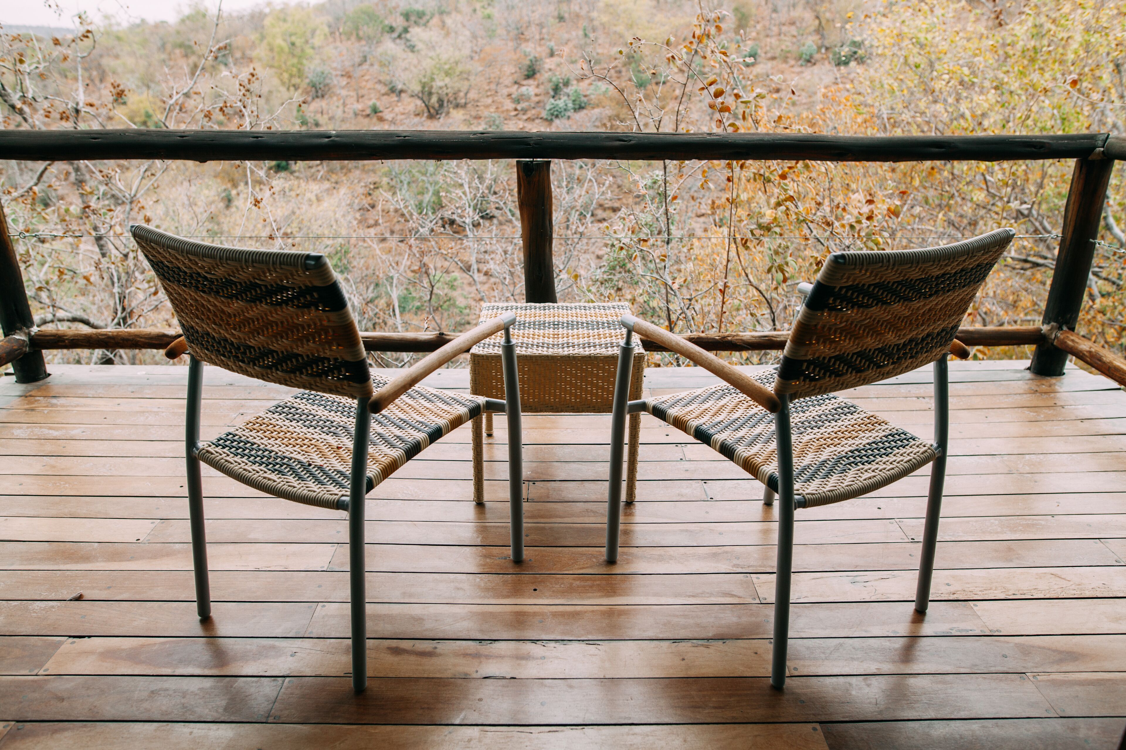 A wooden deck with two wicker chairs and a small table.