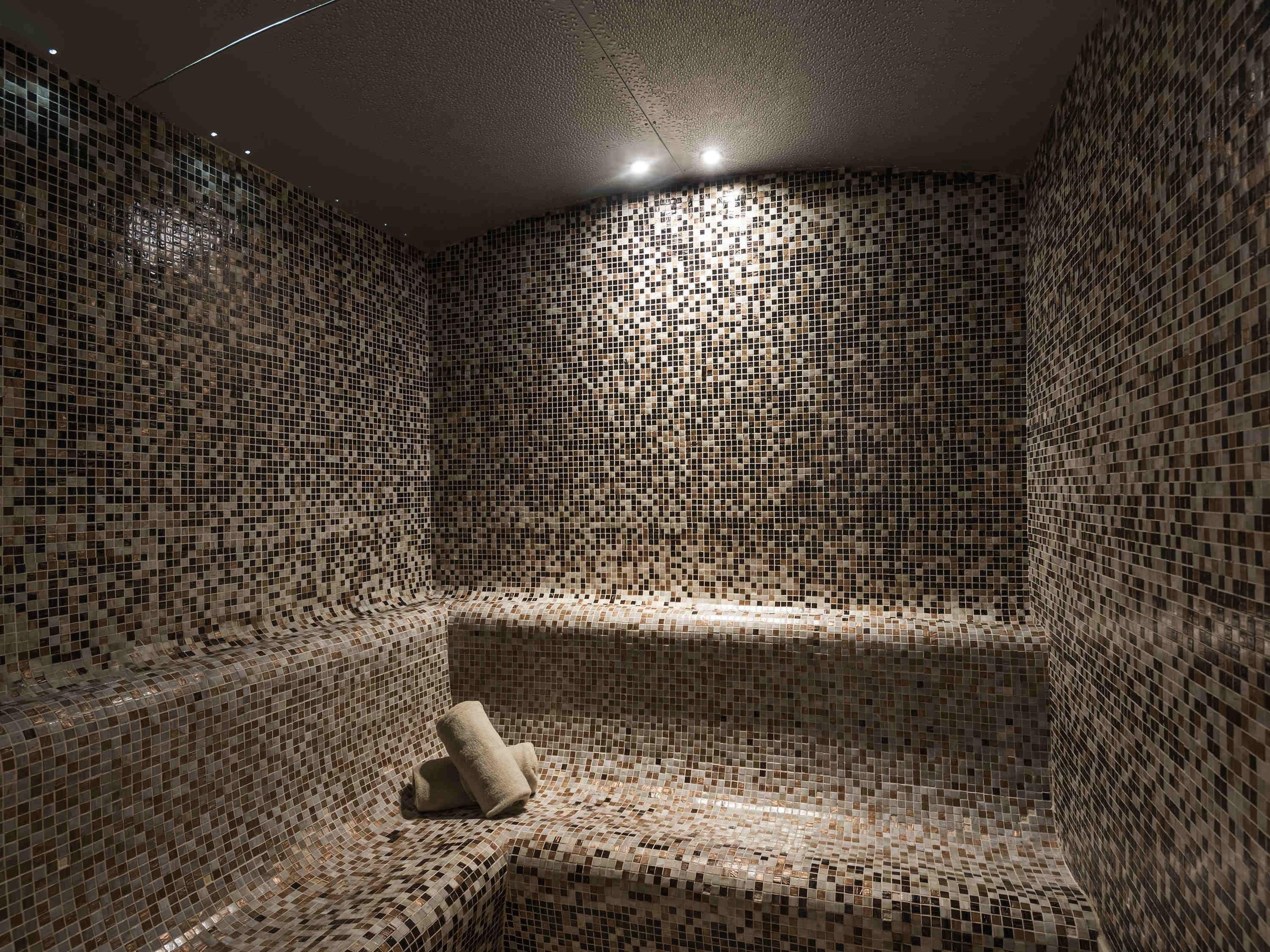 Une pièce dont les murs sont recouverts de mosaïques et qui contient un banc.