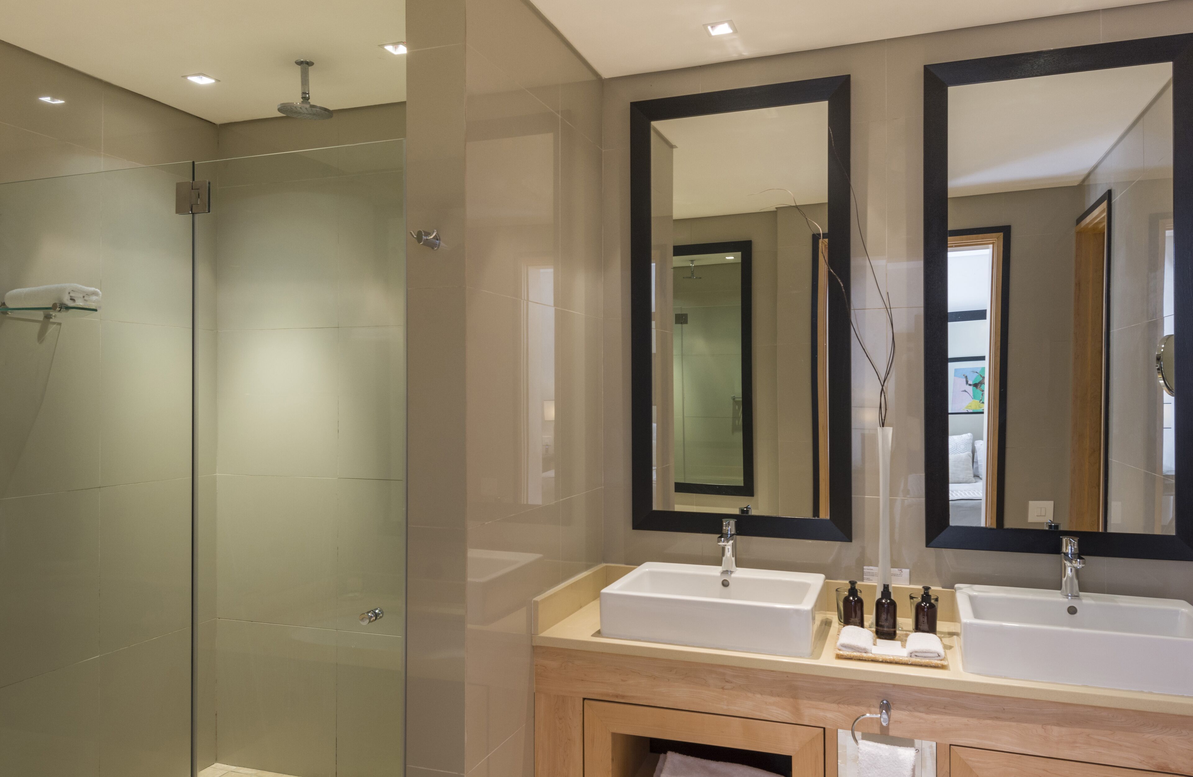 A modern bathroom with a glass-enclosed shower, two sinks, and large mirrors.