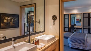 Habitación de hotel moderna con un espejo grande, dos lavamanos, una cama, un escritorio y un armario.
