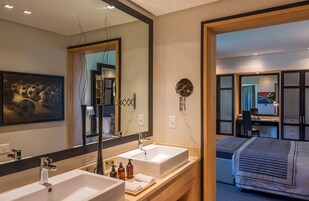 Habitación de hotel moderna con un espejo grande, dos lavamanos, una cama, un escritorio y un armario.