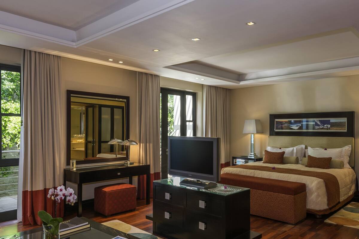 A hotel room with a bed, a TV, a desk with a computer, a dresser, a mirror, and a window with curtains.