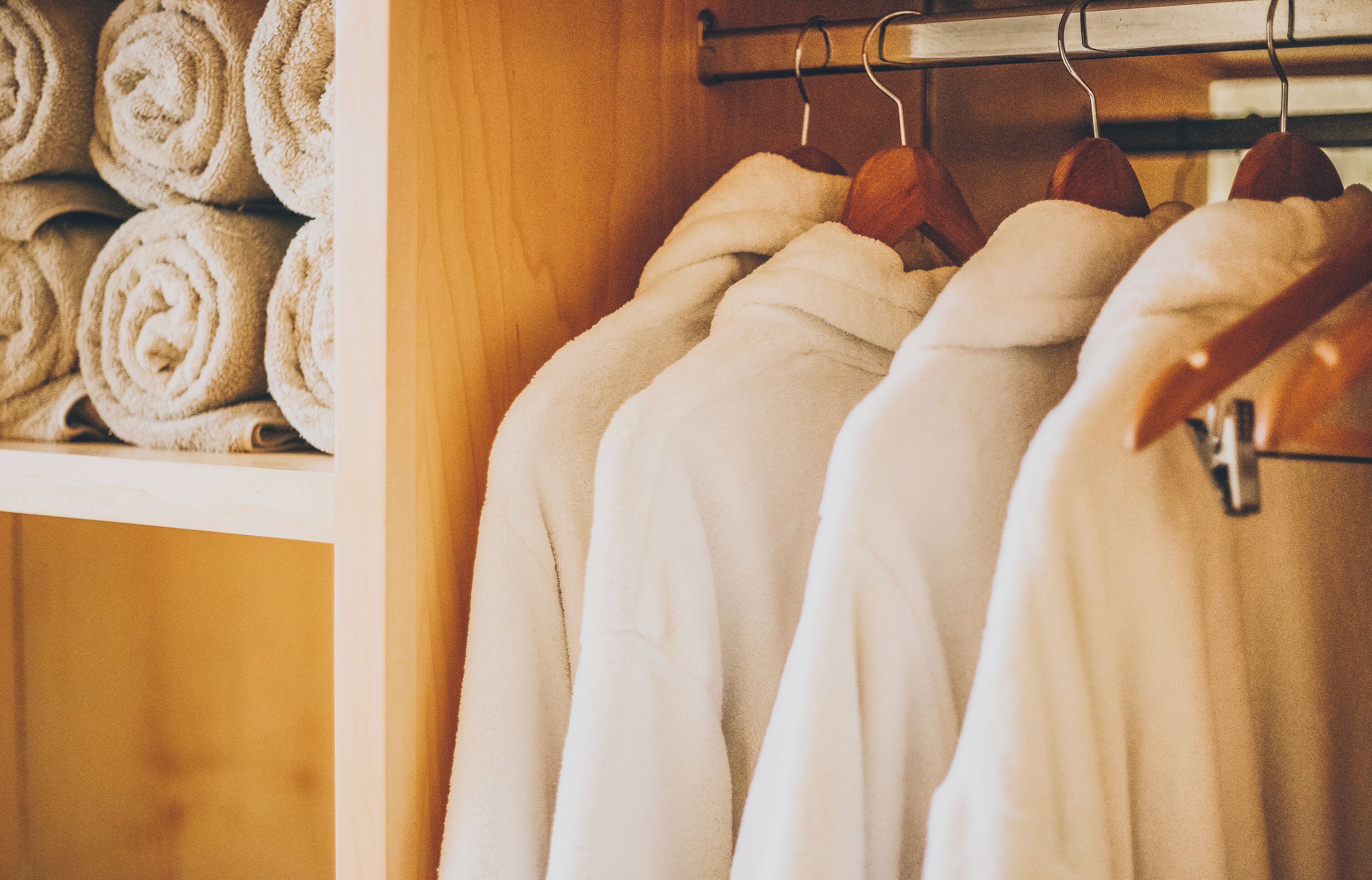 A closet with neatly folded towels and robes on hangers.