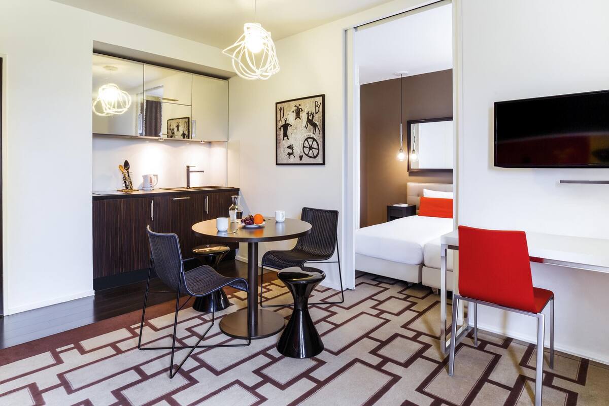Una habitación de hotel moderna con comedor, cocina y televisor montado en la pared.