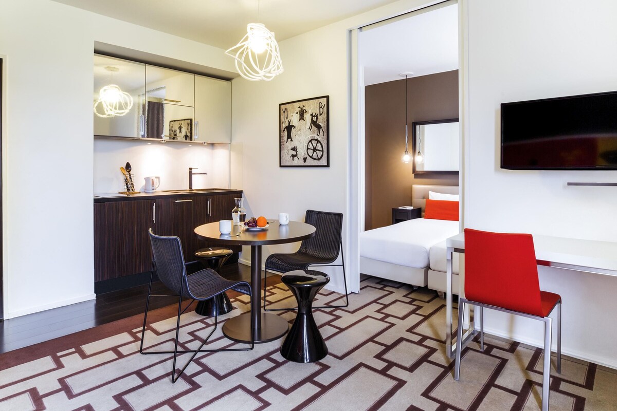 Una habitación de hotel moderna con comedor, cocina y televisor montado en la pared.