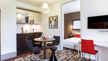 A modern hotel room with a dining area, kitchen, and a TV mounted on the wall.