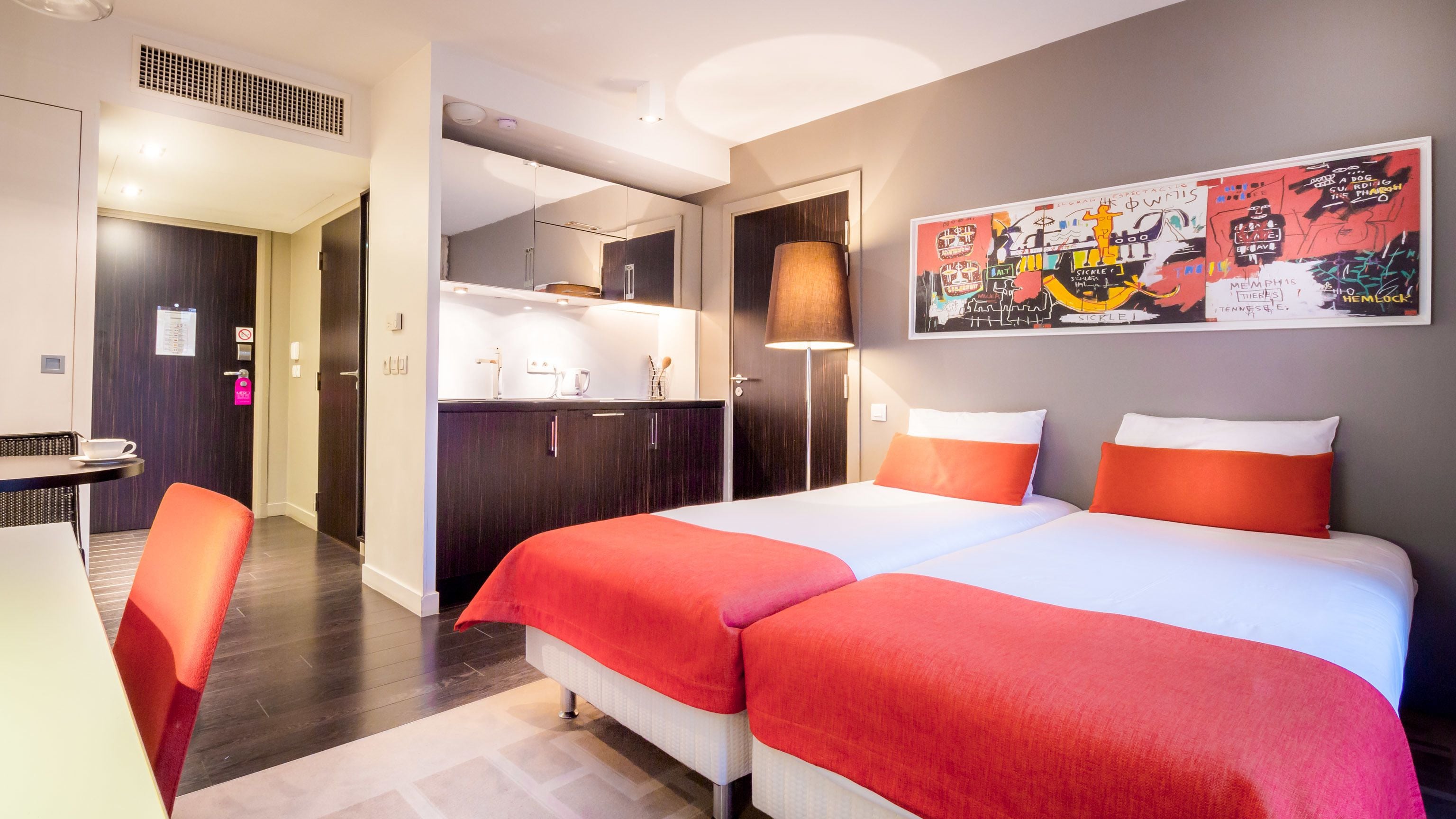 A hotel room with a bed, a desk, a chair, a kitchenette, and a bathroom.