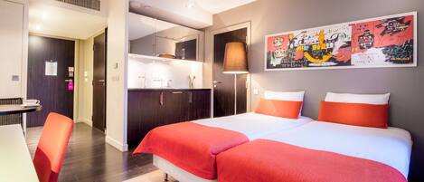 Habitación de hotel con cama, escritorio, silla, kitchenette y baño.