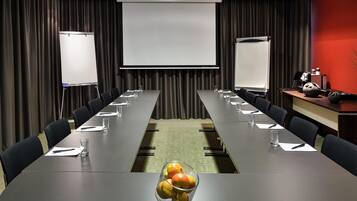 A conference room with a long table, chairs, a projector screen, and a fruit bowl.