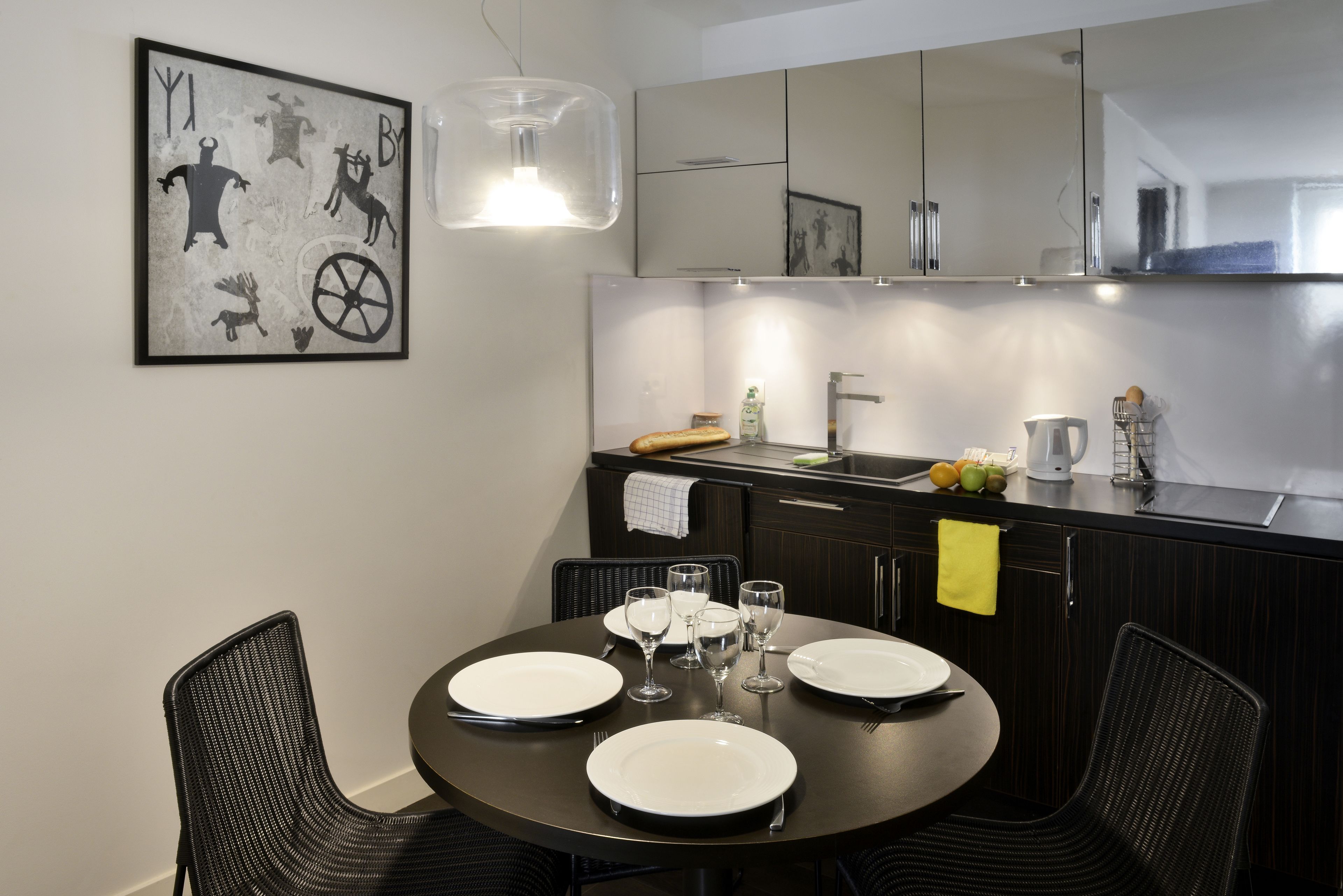 Una cocina moderna con armarios oscuros, una mesa redonda con platos y vasos blancos, y una lámpara colgante.
