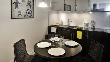 Una cocina moderna con armarios oscuros, una mesa redonda con platos y vasos blancos, y una lámpara colgante.