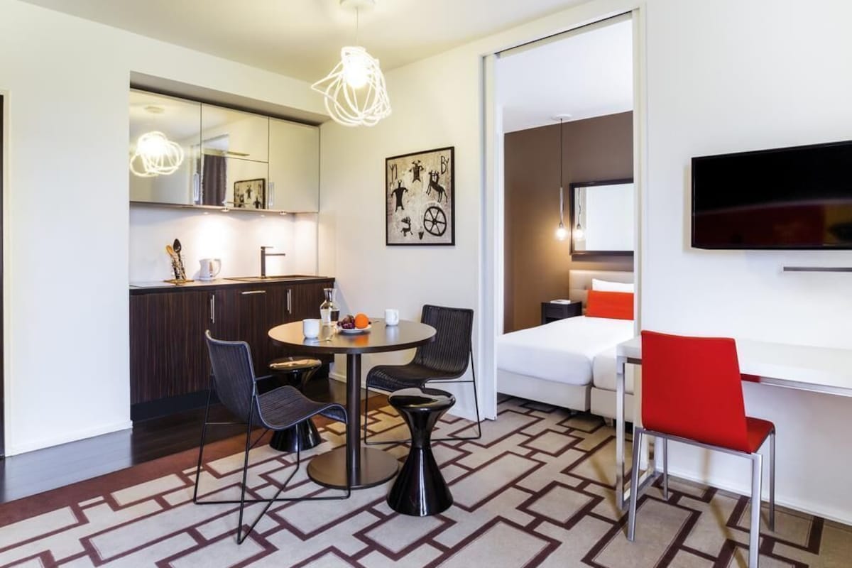 Een compacte hotelkamer met een zithoek, een bed, een televisie en een moderne lamp.
