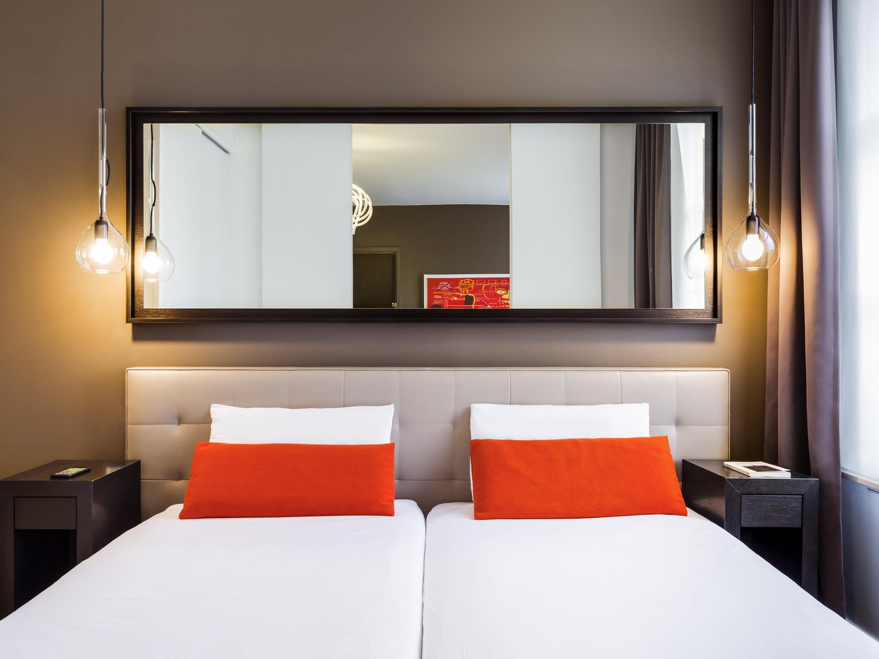 Habitación de hotel con dos camas, un espejo grande y lámparas colgantes.