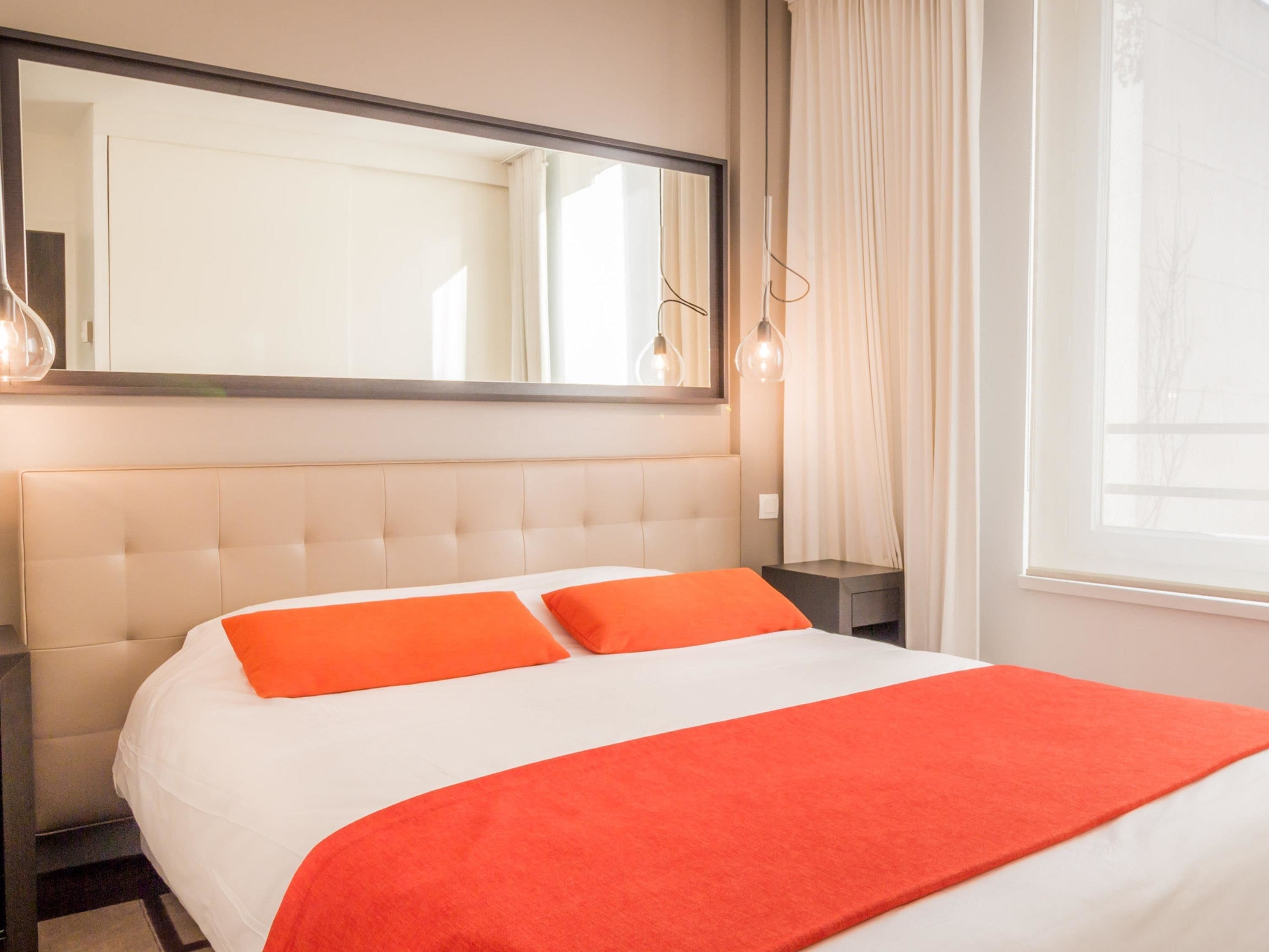 A hotel room with a large bed, a headboard, a nightstand, a mirror, and a window with curtains.
