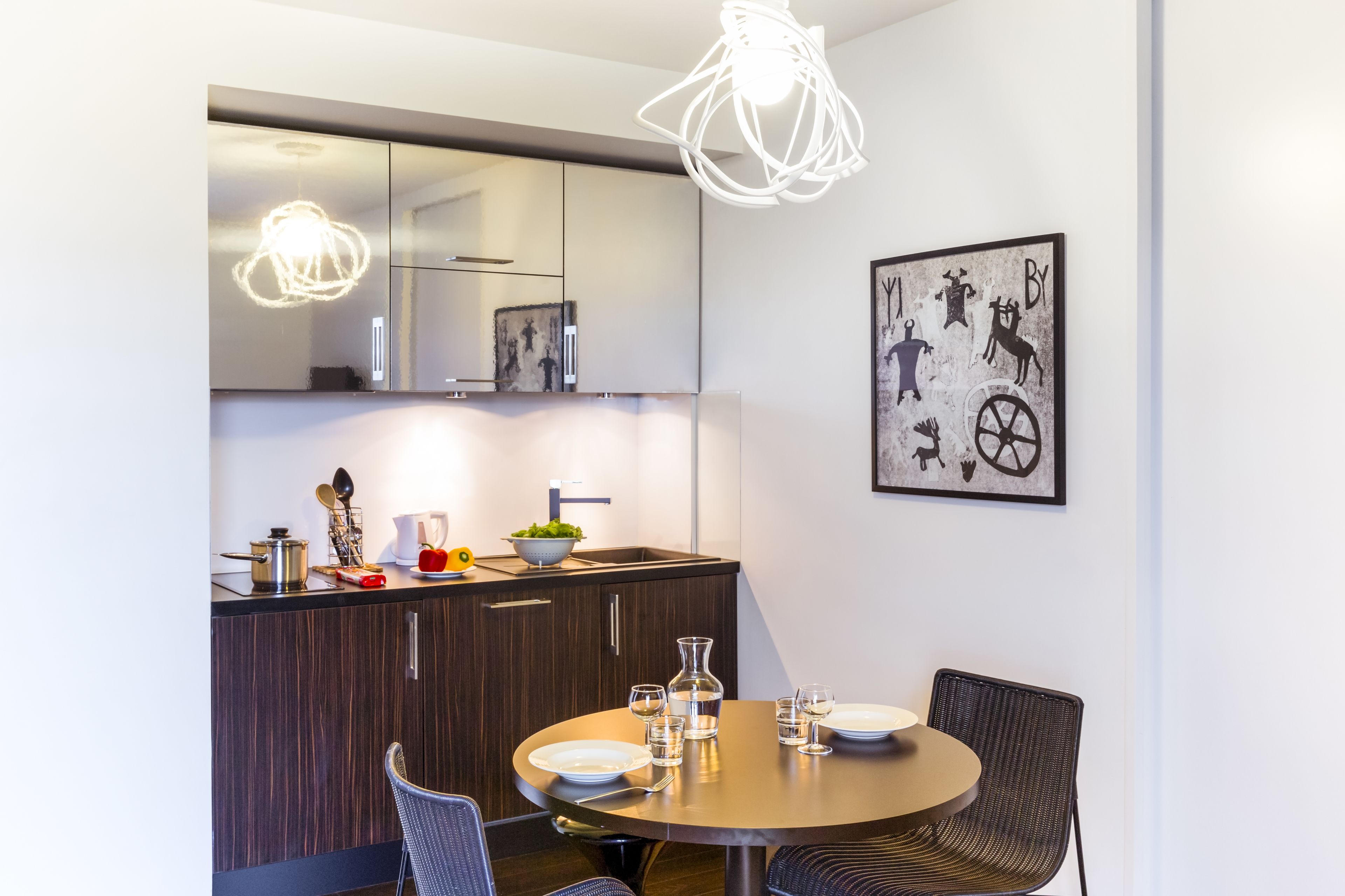 A modern kitchen with dark wood cabinets, a round dining table with chairs, and a hanging light fixture.