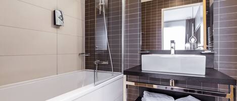 Un baño moderno con una bañera blanca, un tocador negro con un lavabo blanco y un espejo grande sobre el tocador.
