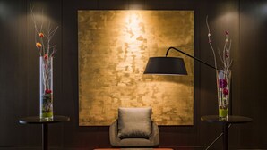 A modern room with a large textured wall, a single grey chair, and two side tables with vases of flowers. - Aparthotel Adagio Grenoble Centre (Grenoble)