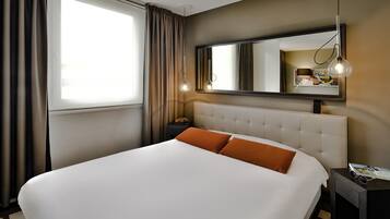 Habitación de hotel con una cama grande, una mesita de noche, un espejo y una ventana con cortinas.