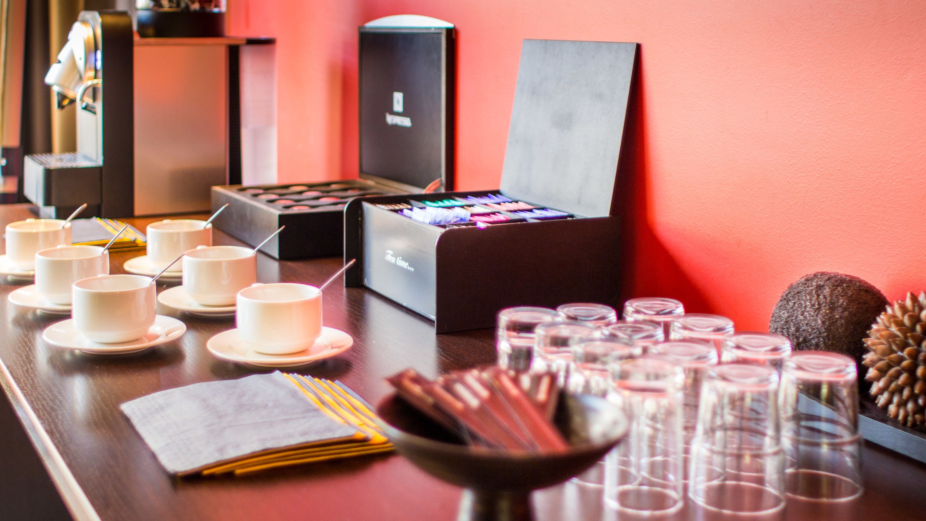 A buffet setup with multiple cups, a box of chocolates, and a variety of small dishes on a table.