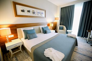 Habitación de hotel con una cama grande, dos mesitas de noche, una silla, un escritorio y una ventana con cortinas.