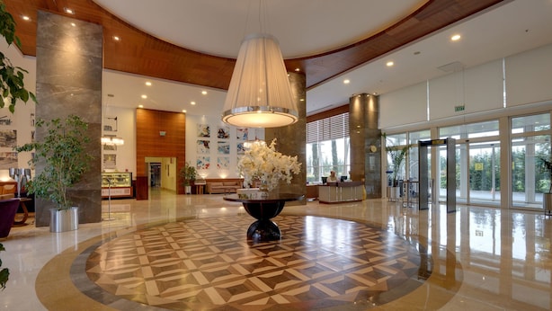 A spacious lobby with a central round table, a reception desk, and a large window providing a view of the outdoors. - Baia Bursa Hotel (Bursa)