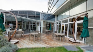 An outdoor patio with wooden flooring, tables, chairs, and green umbrellas. - Baia Bursa Hotel (Bursa)