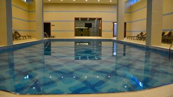 Una piscina interior con agua cristalina, rodeada de sillones de descanso y un suelo de baldosas.
