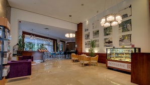 A modern hotel lobby with a reception desk, seating area, and a pastry display. - Baia Bursa Hotel (Bursa)