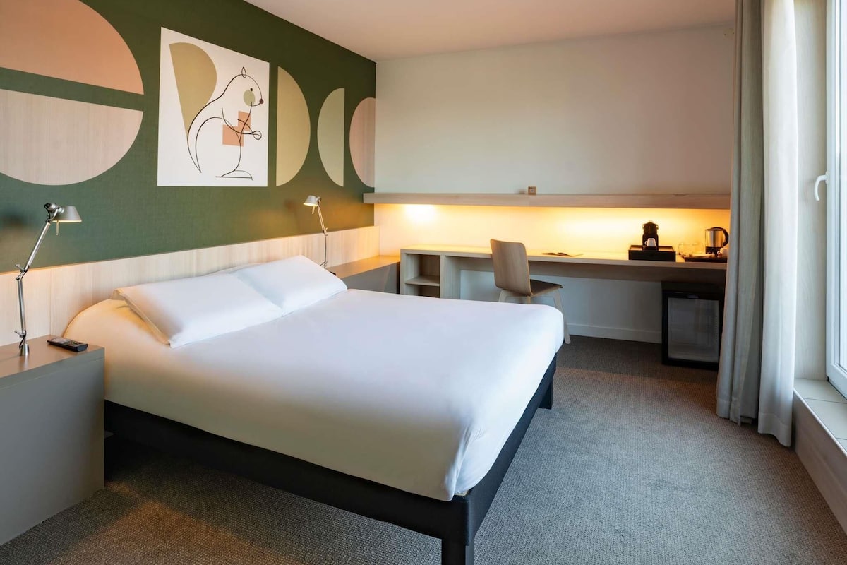 Une chambre d’hôtel comprenant un lit, un bureau, une chaise et un mur orné d’œuvres d’art abstraites.