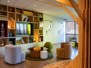 A modern living room with a large flat-screen TV, bookshelves, and comfortable seating. - ibis Styles Guéret (Gueret)