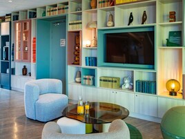 Un salon moderne avec une table basse en verre, des sièges confortables, un téléviseur à écran plat et une bibliothèque remplie de livres et d’objets décoratifs.