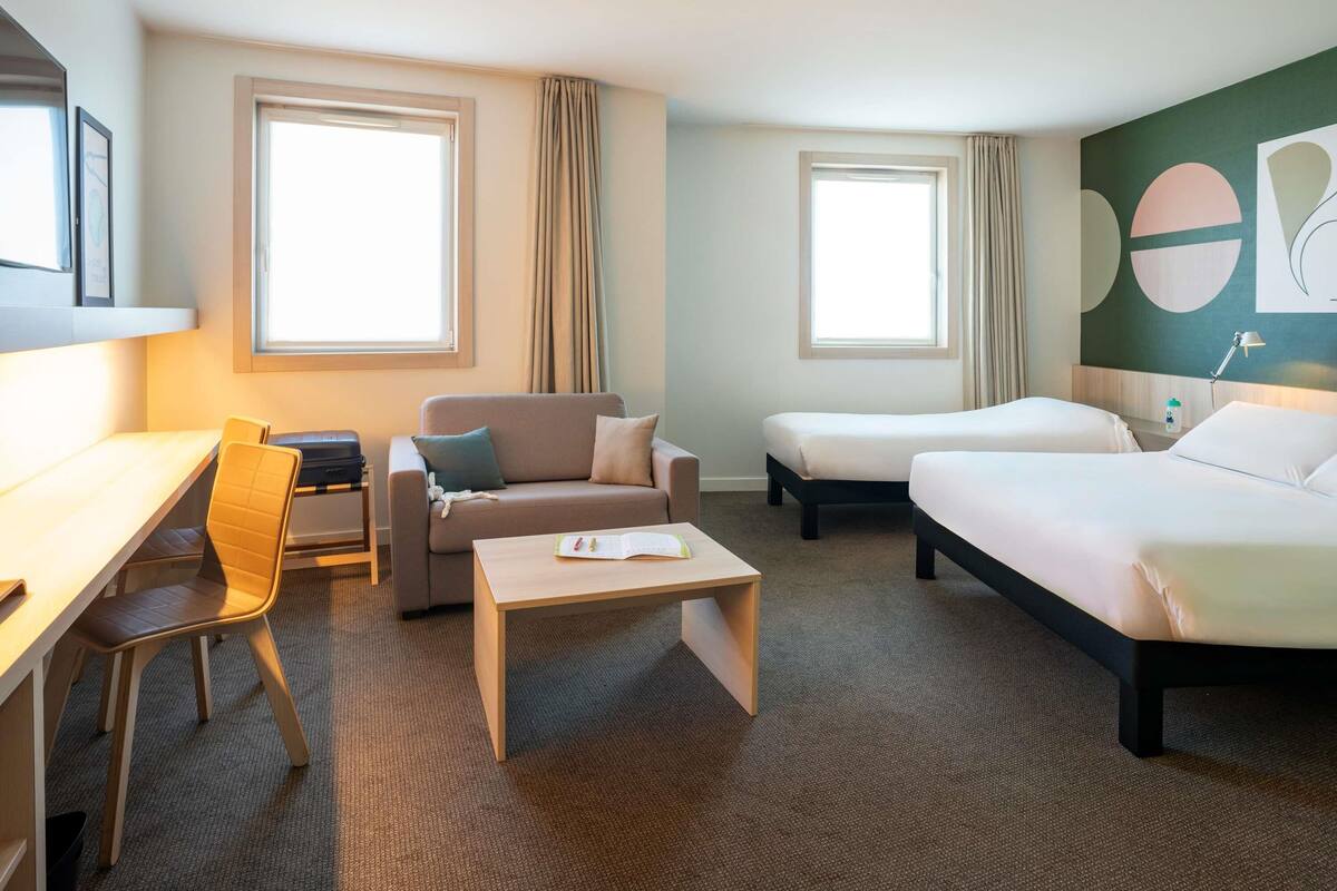 Une chambre d’hôtel équipée d’un bureau, de deux lits, d’un canapé et d’une chaise.