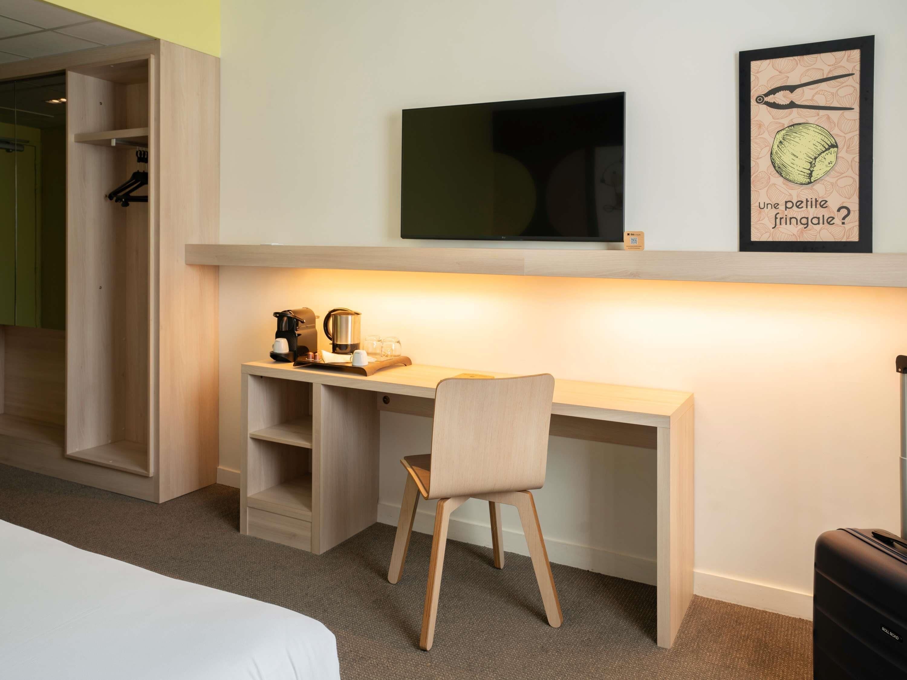 Habitación de hotel con cama, escritorio con silla, televisor y un cuadro en la pared.