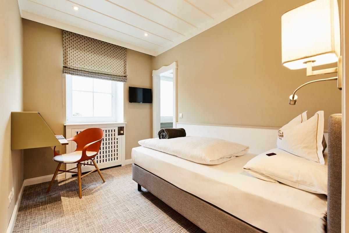A hotel room with a bed, a desk, a chair, a TV, and a lamp.