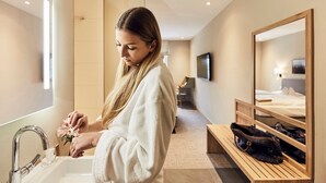 Une salle de bain d’hôtel avec un grand miroir, un lavabo et un banc sur lequel sont posés des sacs.