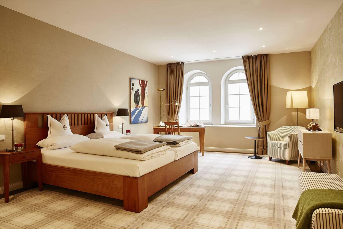 A hotel room with a large bed, a desk, a chair, and a TV.