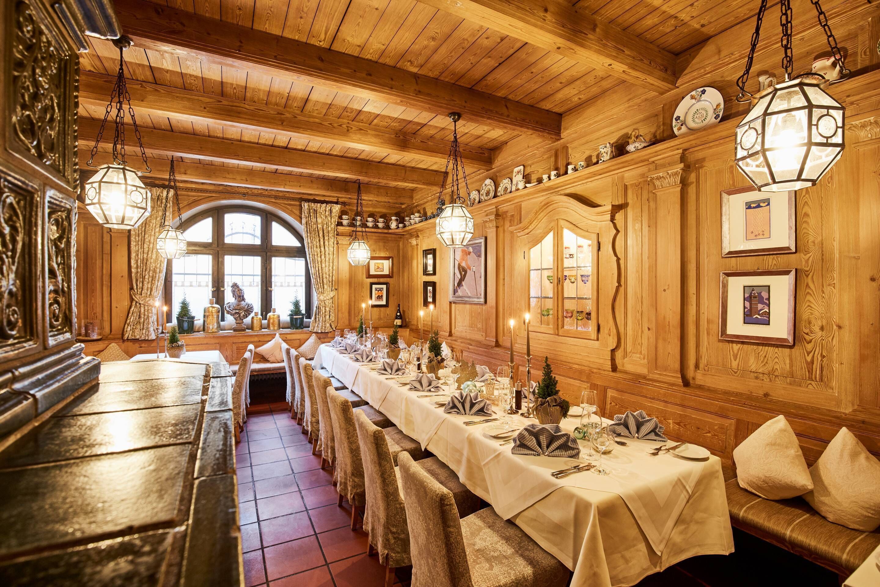 A long dining table set for a formal meal in a wooden interior with hanging lanterns and framed pictures on the walls.