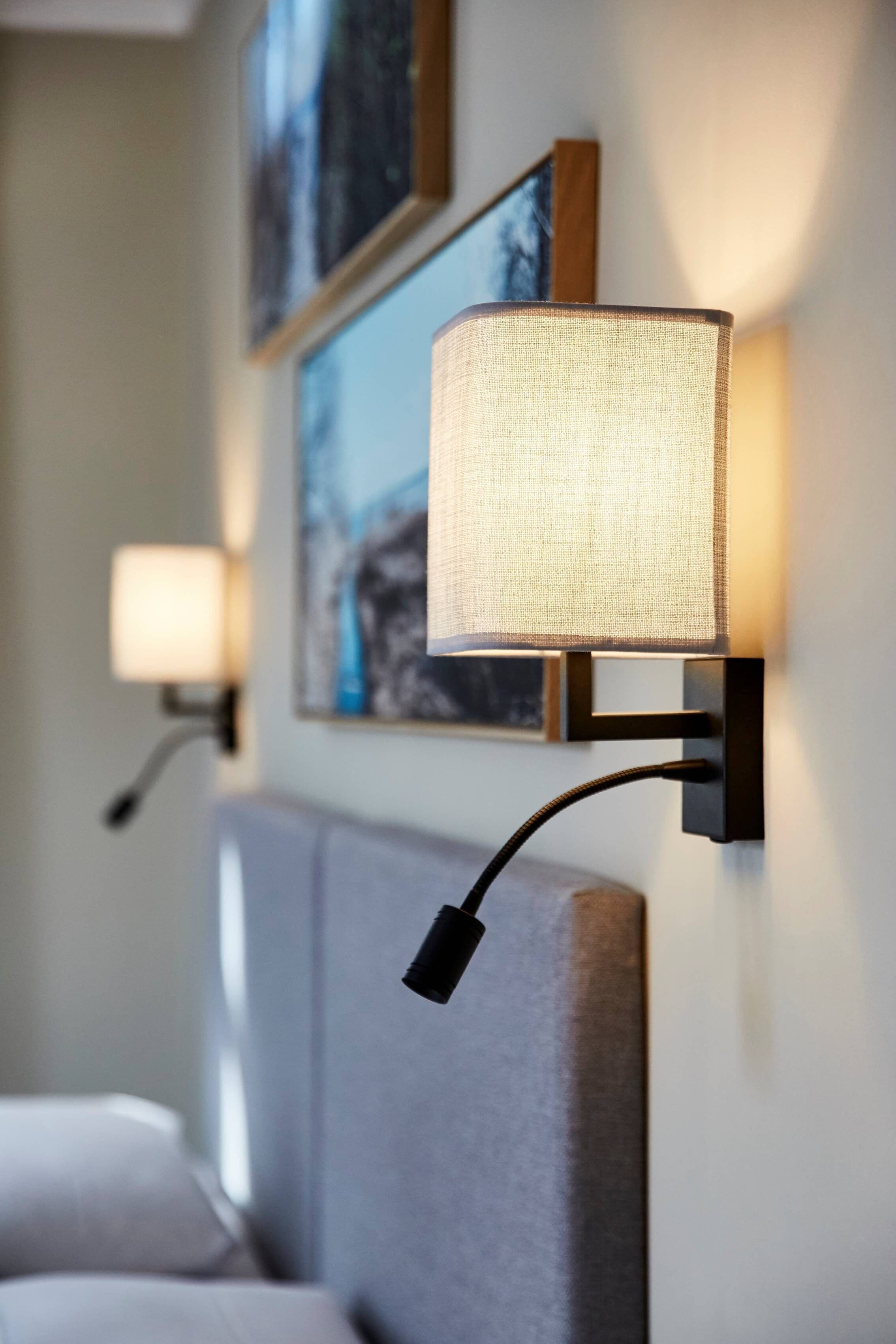 A modern hotel room with a bed, a wall-mounted lamp, and framed artwork.