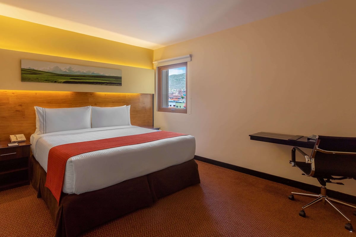 Une chambre d’hôtel avec un lit, un bureau, une chaise, une table de chevet et une fenêtre donnant sur un paysage agréable.