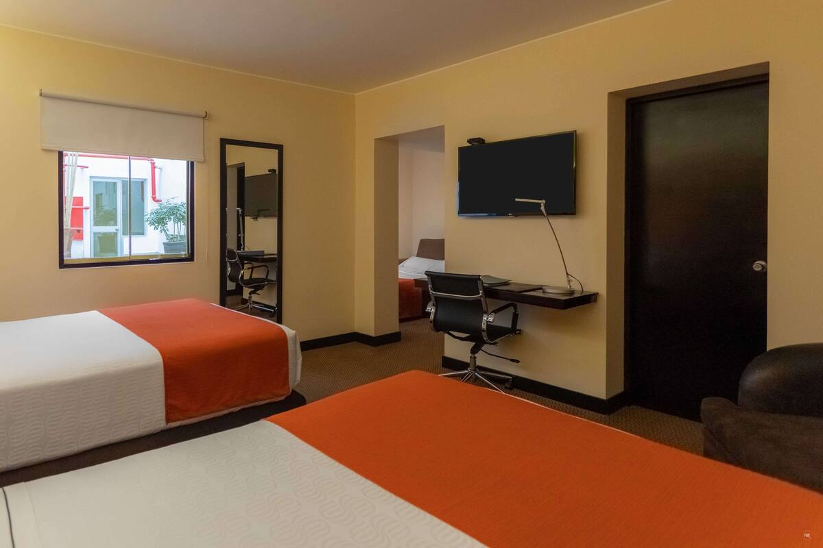 Ein Hotelzimmer mit zwei Betten, einem Schreibtisch mit Stuhl, einem Fernseher und einer Tür.