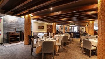 A restaurant with multiple tables and chairs, wooden beams on the ceiling, and a brick pillar.